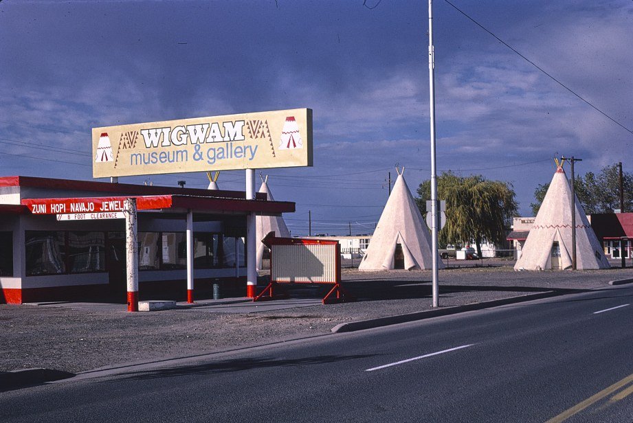 Color photo of the Wigwam motel office and cone-shaped rooms beside a road in Holbrook, Arizona