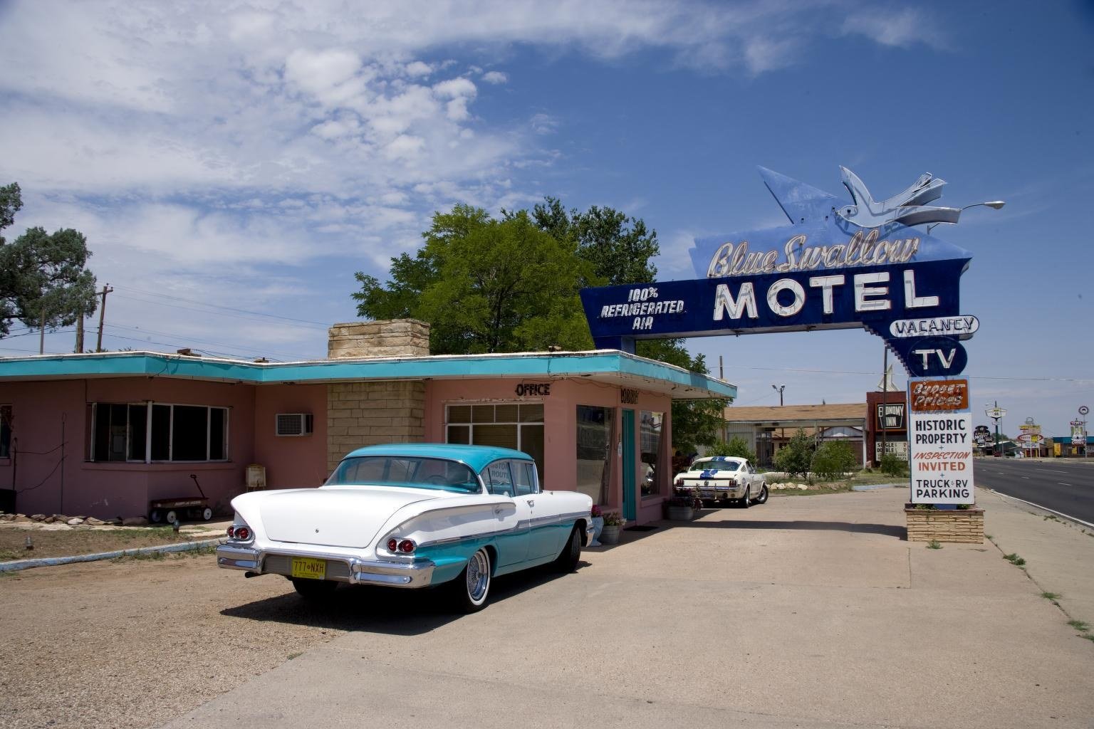 Color photo of the Blue Swallow Motel neon sign and a white 1950s car in Tucumcari, New Mexico